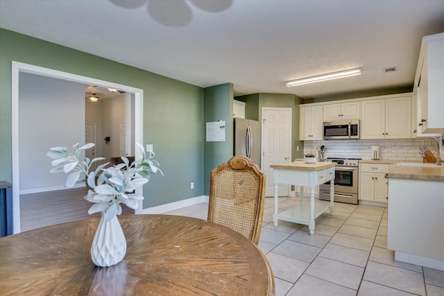 kitchen with decorative backsplash, stainless steel appliances, sink, white cabinets, and light tile patterned flooring