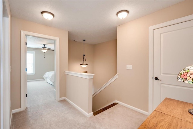 hallway with baseboards, a textured ceiling, an upstairs landing, and light colored carpet