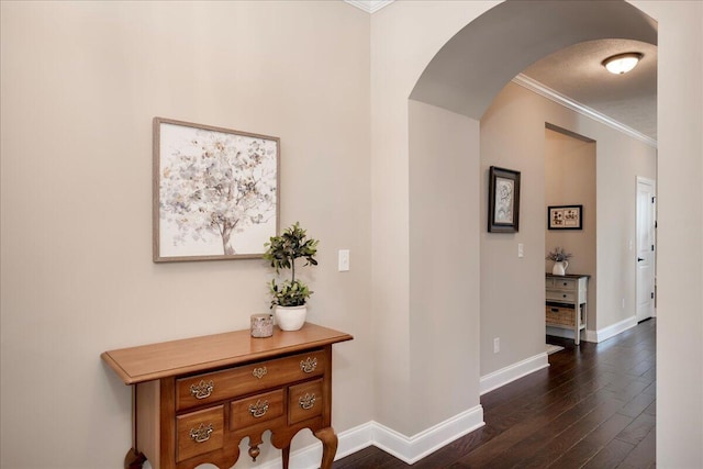 hallway featuring arched walkways, ornamental molding, dark wood-type flooring, and baseboards