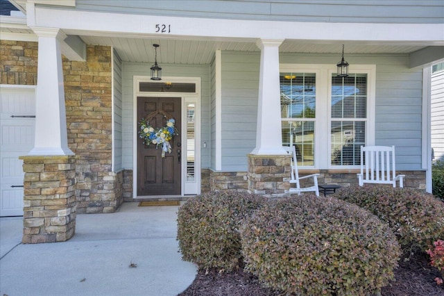 entrance to property with covered porch, stone siding, and a garage