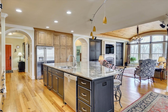 kitchen with appliances with stainless steel finishes, decorative light fixtures, sink, a kitchen island with sink, and light stone counters