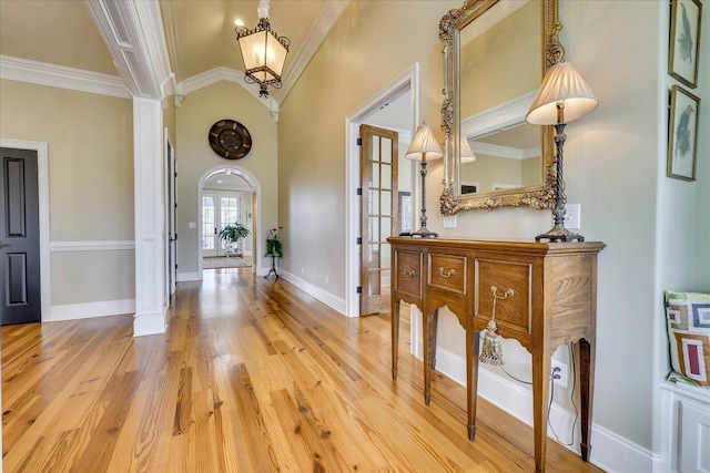 entryway featuring light wood-type flooring, an inviting chandelier, ornamental molding, and decorative columns