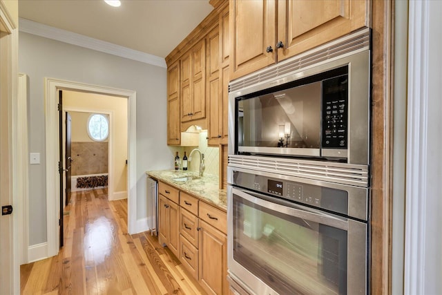 kitchen with sink, light hardwood / wood-style flooring, appliances with stainless steel finishes, ornamental molding, and light stone counters