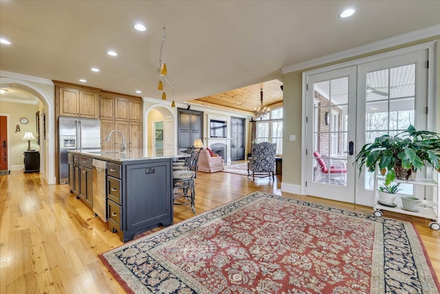 kitchen with a breakfast bar area, appliances with stainless steel finishes, a kitchen island with sink, light stone countertops, and sink