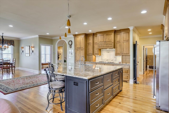 kitchen featuring decorative light fixtures, a large island with sink, light hardwood / wood-style flooring, stainless steel appliances, and light stone counters