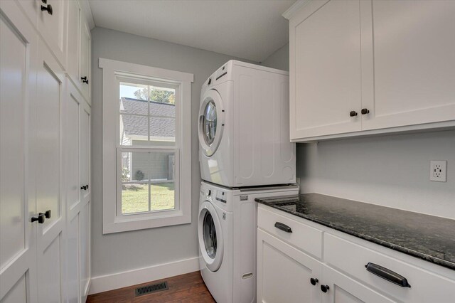 laundry room with cabinets, dark wood-type flooring, and stacked washer and clothes dryer