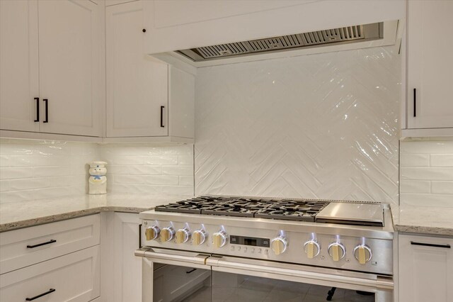 kitchen with backsplash, white cabinets, range hood, gas stove, and light stone counters