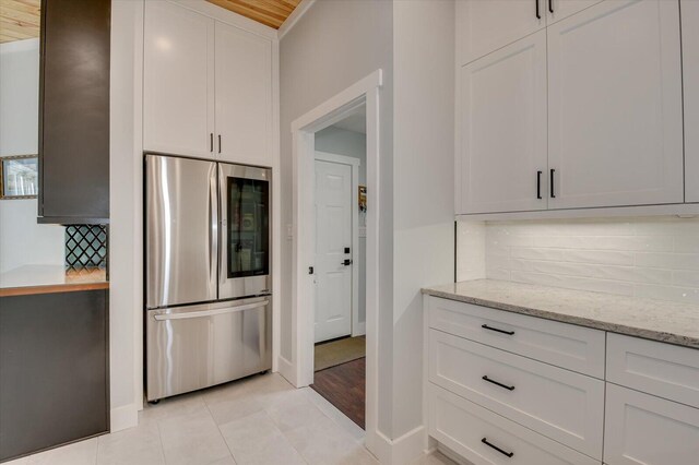 kitchen featuring decorative backsplash, stainless steel fridge, white cabinets, and light stone counters