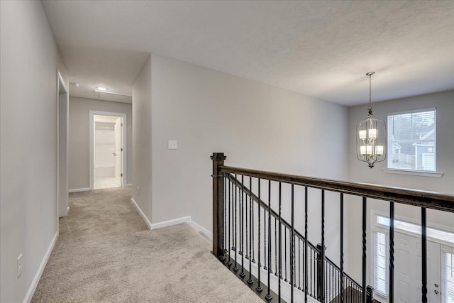 hallway featuring light colored carpet and a notable chandelier