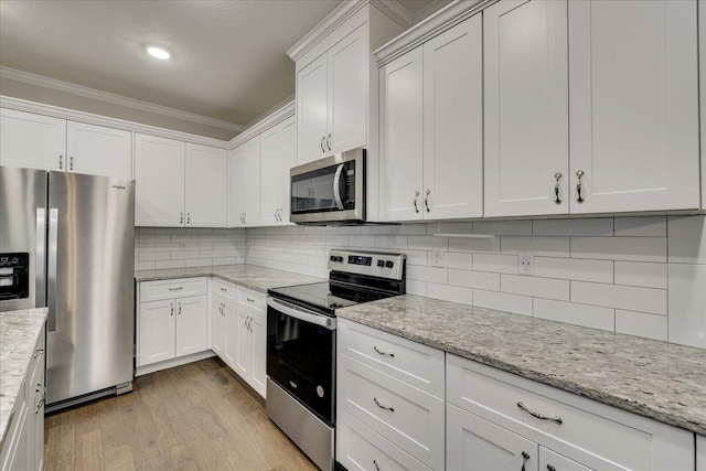 kitchen with appliances with stainless steel finishes, white cabinetry, tasteful backsplash, light stone countertops, and light hardwood / wood-style floors