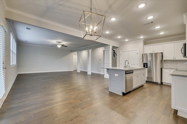 kitchen with stainless steel appliances, an island with sink, white cabinets, and decorative light fixtures