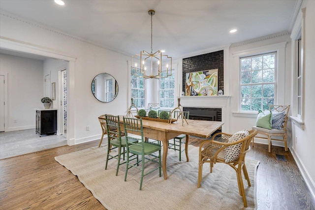 dining space with an inviting chandelier, hardwood / wood-style flooring, a brick fireplace, and ornamental molding