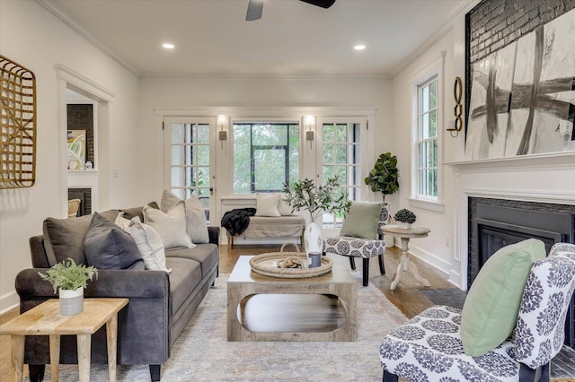 living room featuring light wood-type flooring, a large fireplace, ceiling fan, and crown molding