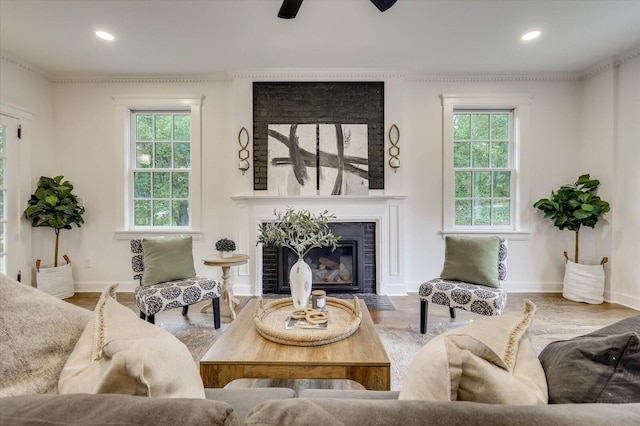 living room featuring ceiling fan, crown molding, wood-type flooring, and a brick fireplace