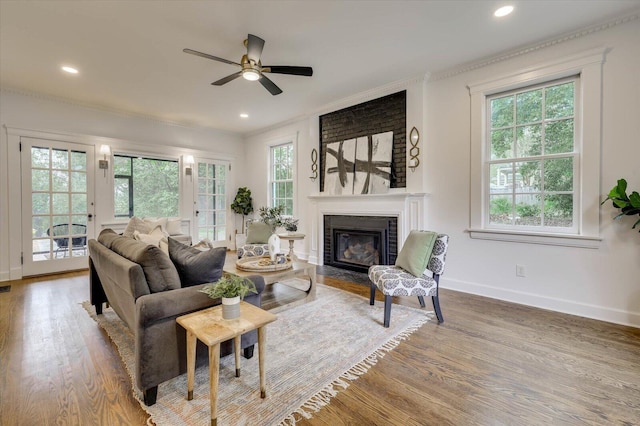 living room with hardwood / wood-style flooring, ceiling fan, crown molding, and a brick fireplace