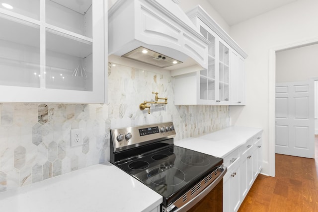 kitchen featuring backsplash, stainless steel range with electric stovetop, custom exhaust hood, dark hardwood / wood-style floors, and white cabinetry