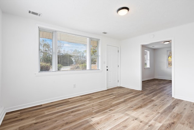 empty room featuring light wood-style floors, visible vents, plenty of natural light, and baseboards