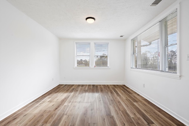 empty room featuring baseboards, a textured ceiling, visible vents, and wood finished floors