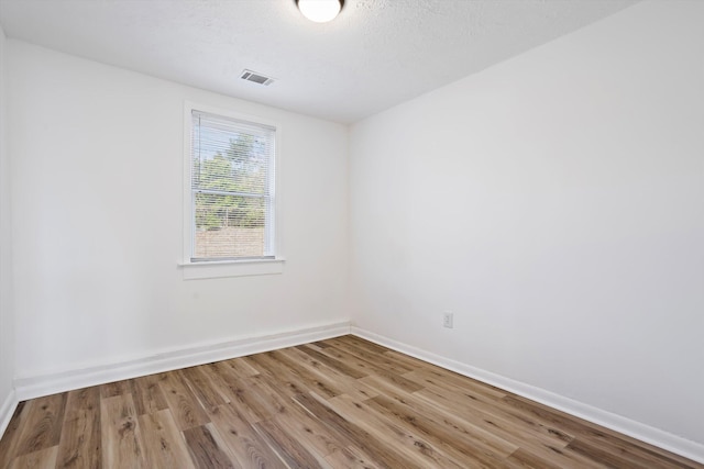 empty room featuring visible vents, a textured ceiling, baseboards, and wood finished floors