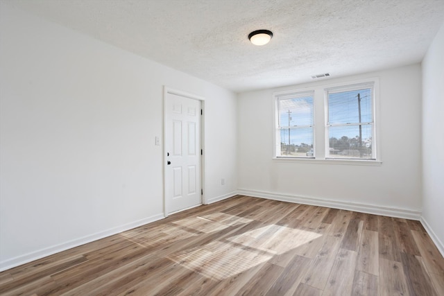 unfurnished room with visible vents, light wood-style flooring, baseboards, and a textured ceiling