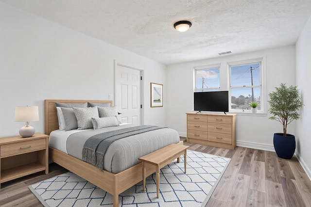 bedroom featuring a textured ceiling, light wood-style flooring, visible vents, and baseboards