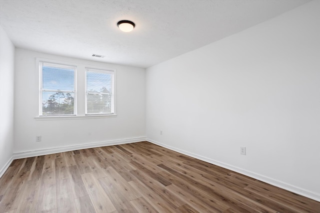 unfurnished room with visible vents, light wood-style flooring, baseboards, and a textured ceiling