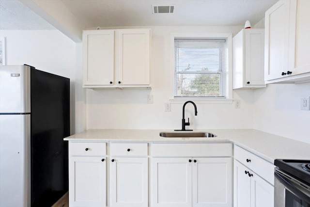 kitchen with freestanding refrigerator, white cabinets, light countertops, and a sink