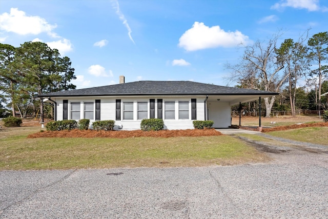 ranch-style home with a chimney, a shingled roof, an attached carport, driveway, and a front lawn