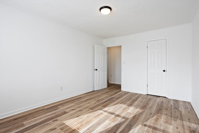 unfurnished bedroom with light wood-type flooring, a textured ceiling, and baseboards