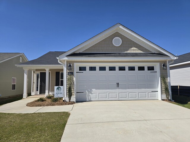 view of front of property featuring covered porch, a garage, and a front lawn