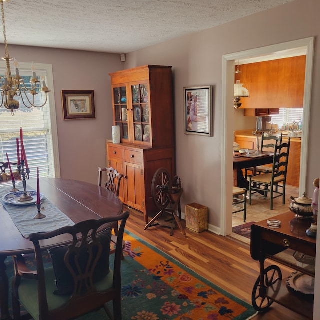 dining space with light wood-style flooring, a notable chandelier, baseboards, and a textured ceiling