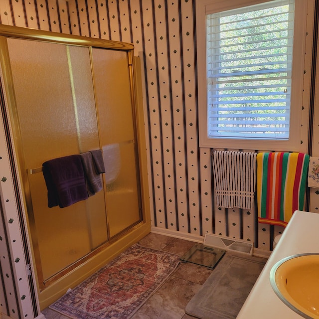 bathroom featuring baseboards, wallpapered walls, a stall shower, a sink, and tile patterned flooring