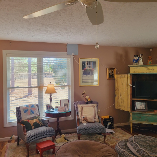 living area with a textured ceiling, baseboards, and a ceiling fan