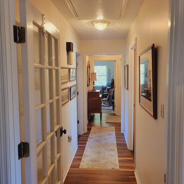 corridor featuring attic access, dark wood-style floors, and a textured ceiling