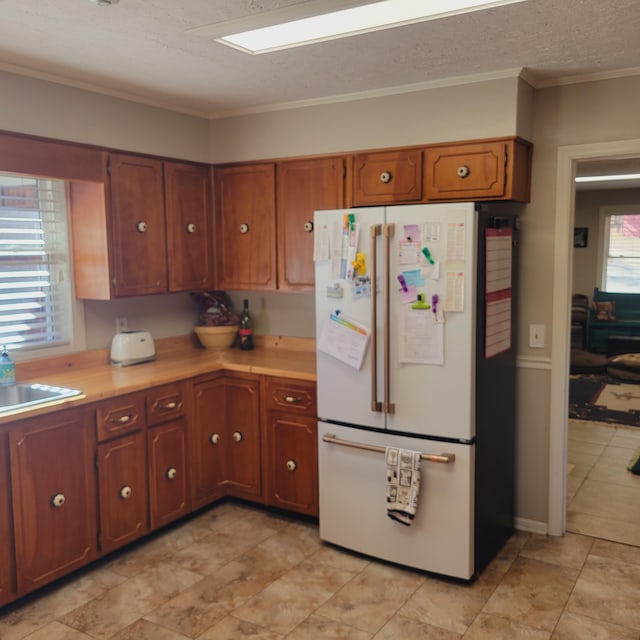 kitchen featuring a sink, a textured ceiling, freestanding refrigerator, crown molding, and light countertops