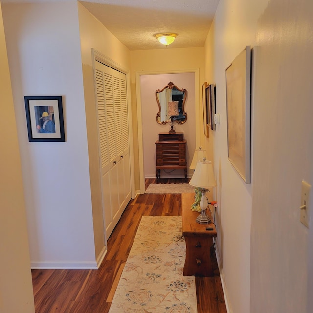 hall with dark wood-style floors, baseboards, and a textured ceiling