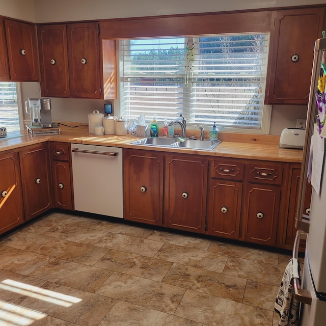 kitchen with light countertops, stone finish flooring, white dishwasher, and a sink