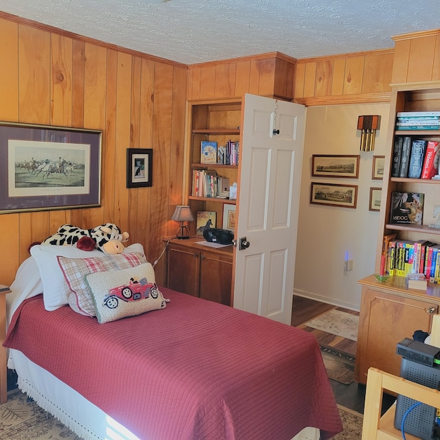 bedroom with wooden walls, a textured ceiling, and wood finished floors