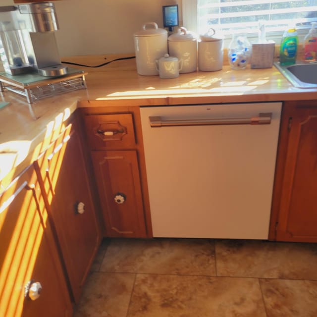 kitchen with light tile patterned floors, a sink, light countertops, and white dishwasher