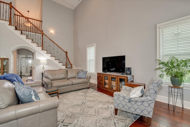 living room featuring hardwood / wood-style flooring, a towering ceiling, plenty of natural light, stairway, and baseboards