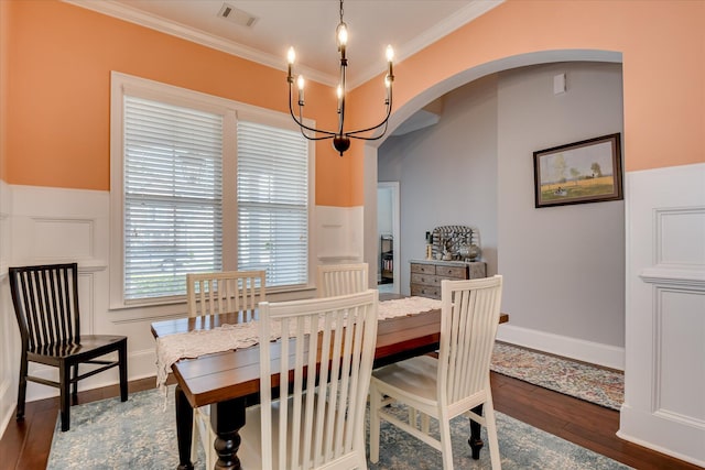 dining space featuring arched walkways, ornamental molding, dark wood finished floors, a chandelier, and a wainscoted wall