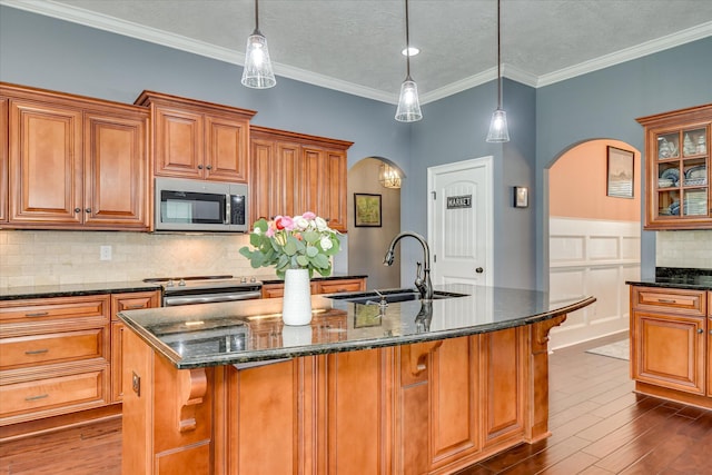 kitchen with appliances with stainless steel finishes, arched walkways, a sink, brown cabinets, and ornamental molding