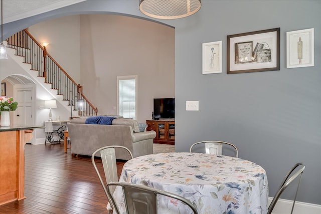 dining space with arched walkways, stairway, dark wood finished floors, and a high ceiling