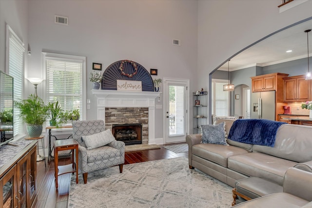 living room with a towering ceiling, wood-type flooring, arched walkways, a fireplace, and crown molding