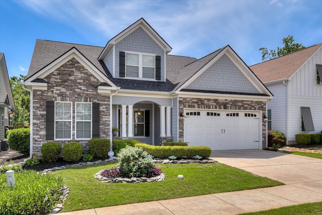craftsman-style home with stone siding, a shingled roof, a front yard, and driveway