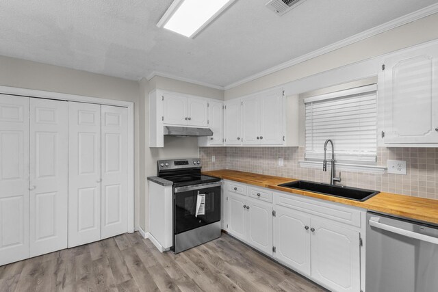 kitchen with appliances with stainless steel finishes, tasteful backsplash, sink, white cabinetry, and butcher block counters