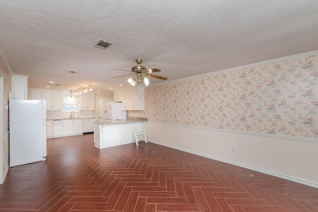 unfurnished living room with ceiling fan, dark parquet flooring, sink, and crown molding