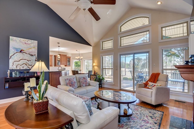 living area featuring high vaulted ceiling, light wood-style flooring, visible vents, and ceiling fan with notable chandelier