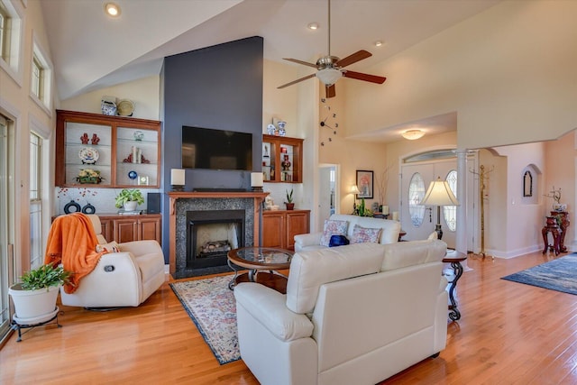 living area featuring high vaulted ceiling, light wood-style flooring, decorative columns, and a fireplace with flush hearth