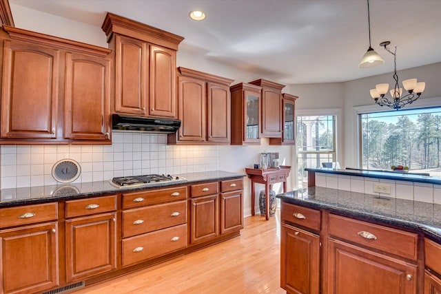 kitchen featuring brown cabinets, decorative light fixtures, stainless steel gas cooktop, light wood-style floors, and under cabinet range hood